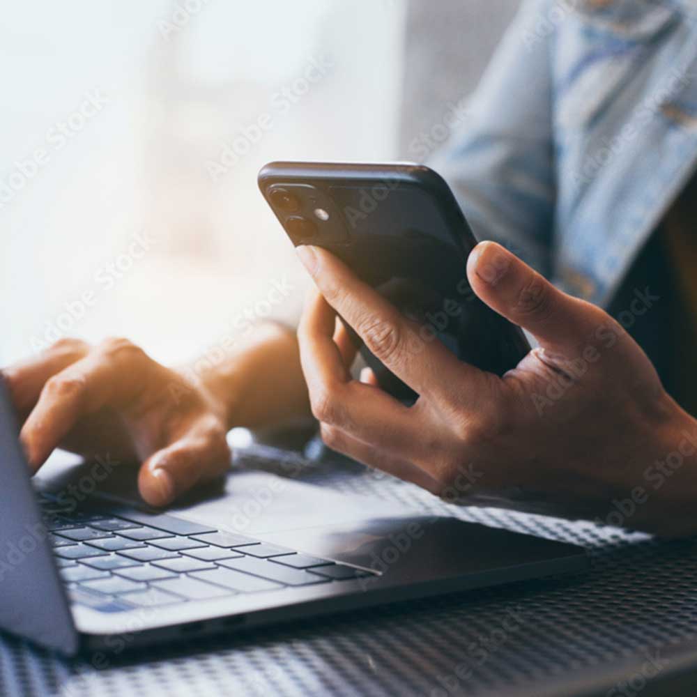 Man sitting at a desk with laptop and phone in his hand looking to contact PSPS